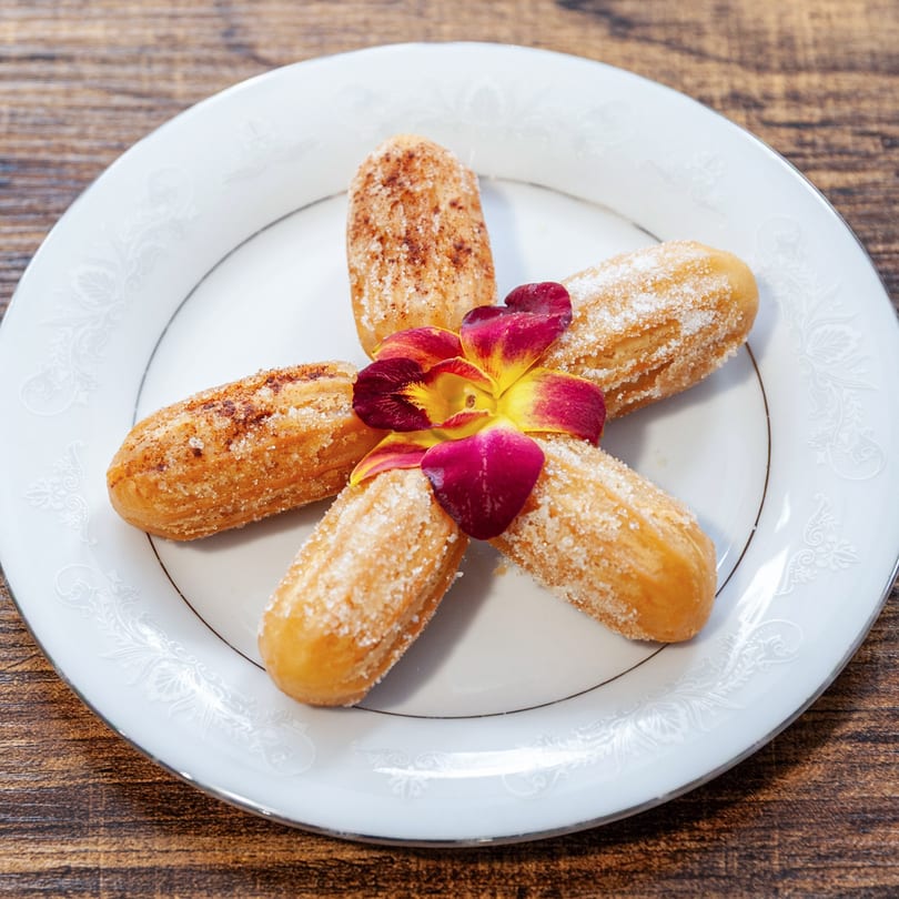 Five Dulce Bakery churros, some with cinnamon sugar, arranged around a vibrant red and yellow flower.
