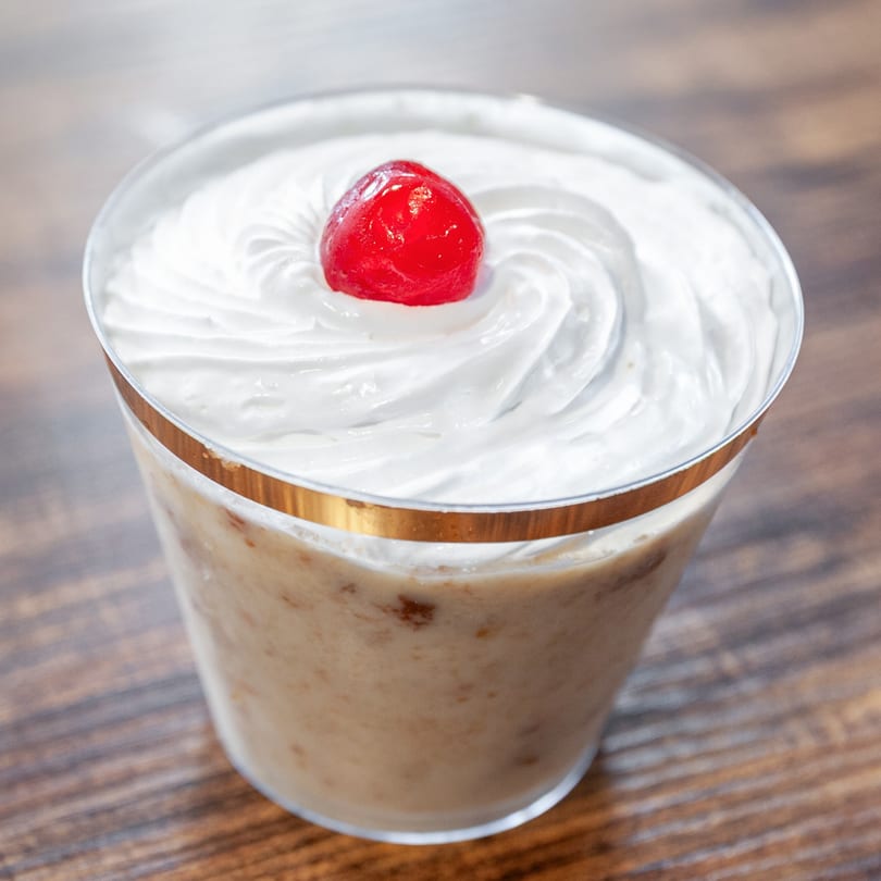 Dulce Bakery's creamy dessert cup with whipped topping and a bright red cherry on a wooden table.