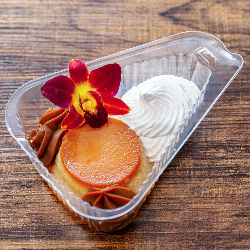 Flan dessert with caramel, whipped cream, and a red orchid in a clear plastic container.