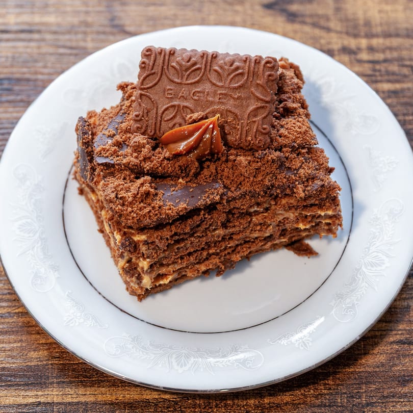 A slice of Dulce Bakery's chocolate cake with dulce de leche and a cookie on a white plate.