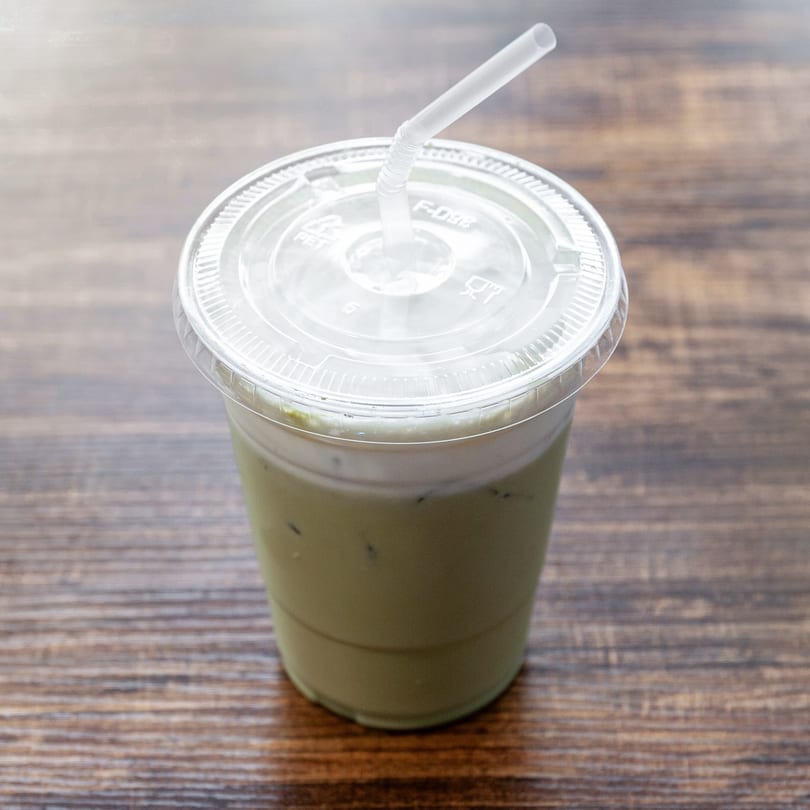 Iced matcha latte with a clear lid and straw, on a wooden table at Dulce Bakery.